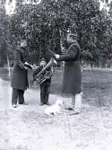 Foto av officerarna Södersten och Michelson samt en ung pojke som håller i en stor tuba, troligen är han en del av musikkåren, samt en hund som ligger lugnt på marken mellan männen och pojken. Text i album: 