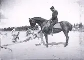 Foto av en man i uniform som sitter på en häst vid en strand där ett gäng militärer tar sig ett bad. Text i album: 