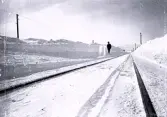 Foto av ett snötäckt järnvägsspår med en man som står vid spåret samt att man kan skönja berg i bakgrunden.