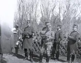 Foto av en grupp militärer som står och diskuterar strategier, möjligtvis, med ett staket och träd i bakgrunden. Text i album: 