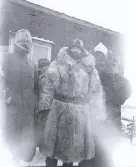 Foto av påpälsade militärer under arméfördelningens fältövningar 1905, i bakgrunden syns en byggnad. Text i album: