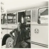 En chaufför i kavaj poserar vid sidan av en SJ-buss, trol. i närheten av järnvägsstationen, Växjö.