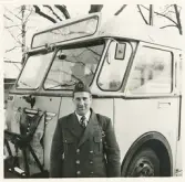 En chaufför i uniform och båtmössa står framför en SJ-buss, trol. i närheten av järnvägsstationen, Växjö.