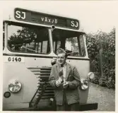 En chaufför i kavaj, slips och båtmössa står framför en SJ buss, trol. i närheten av järnvägsstationen, Växjö.