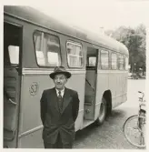 En äldre man i kostym och hatt poserar vid sidan av en SJ-buss, trol. på busstorget/järnvägsplan framför järnvägsstationen, Växjö.