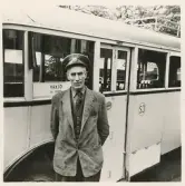 En chaufför i kavaj med väst, slips och skärmmössa står invid en SJ-buss, trol. på busstorget/järnvägsplan vid järnvägsstationen, Växjö.