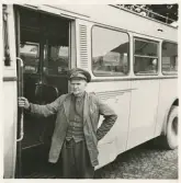 En chaufför i kavaj med väst, slips och skärmmössa står invid en SJ-buss, trol. på busstorget/järnvägsplan vid järnvägsstationen, Växjö.