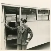 En chaufför i kavaj och skärmmössa står invid en SJ-buss, trol. på busstorget/järnvägsplan vid järnvägsstationen, Växjö.