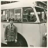 En chaufför i kavaj och skärmmössa står invid en SJ-buss, trol. på busstorget/järnvägsplan vid järnvägsstationen, Växjö.