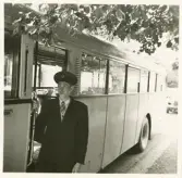 En chaufför i kavaj med väst, slips och skärmmössa står invid en SJ-buss, trol. vid busstorget/järnvägsplan vid järnvägsstationen, Växjö.