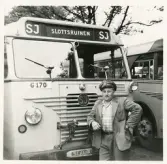 En chaufför i rutig skjorta, kavaj och skärmmössa står invid en SJ-buss, trol. på busstorget/järnvägsplan vid järnvägsstationen, Växjö.