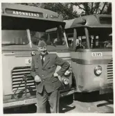 En chaufför i uniformskavaj, slips och båtmössa poserar framför några SJ-bussar , trol. på busstorget/järnvägsplan i Växjö.