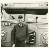 En chaufför i jacka, slips och båtmössa står framför en stadsbuss , någonstan i Växjö.