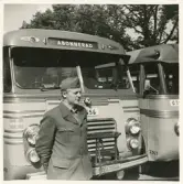 En chaufför i kavaj och båtmössa står framför några SJ-bussar , trol. på busstorget/järnvägsplan i Växjö.