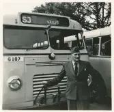 En chaufför i kavaj och båtmössa poserar framför några SJ-bussar, trol. på busstorget/järnvägsplan i Växjö.