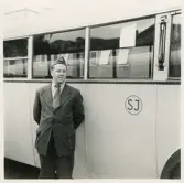 En chaufför i kavaj, slips och båtmössa poserar bredvid en SJ-buss, trol. i Växjö.