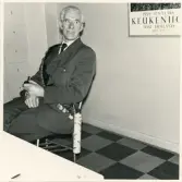 En leende man i busschaufförsuniform utrustad med diverse dekorationer. Han sitter med pipa i handen, trol. vid någon form av avtackning.
Busschaufför Nils Linderholm, Växjö.