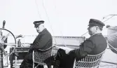 Två män med skepparmössor ombord på ångjakten Tritonia. Text i album: 
