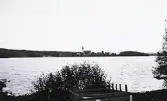 Bild över en sjö taget från en strandkant och med en kyrka och kust i bakgrunden. Text i album: 