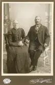 Ett äldre par poserar för fotografen. Mannen har en förtjänstmedalj med Oscar II:s bild i band runt halsen.
Helfigur. Ateljéfoto.
