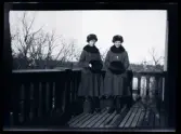 Systrarna Elsa och Gudrun i likadana ytterkläder, porträtterade på balkongen till familjen Morthensens villa Solveden, Djursholm.
