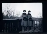 Systrarna Elsa och Gudrun i likadana ytterkläder, porträtterade på balkongen till familjen Morthensens villa Solveden, Djursholm.