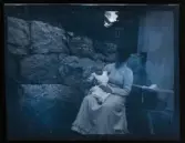 En kvinna sitter utanför ett hus med ett spädbarn i knät.