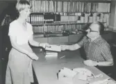Till höger bakom disken sitter föreståndare/bibliotikarie Ivar Andersson, Kållereds bibliotek 1970-tal. Framför disken står kunden Barbro Holm.