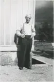 Fredrik Larsson (1874 - 1961), klädd i hängslen, står vid sin husgavel Sporred 1:8 