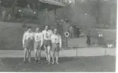 Löpare från KSK (Kållereds sportklubb) där fyra idrottsklädda män/ungdomar står uppställda bredvid varandra på en gräsmatta, okänd plats och årtal. Från vänster: 1. Troligtvis Gösta Ekstedt. 2. Okänd. 3 Troligtvis Arne Andersson (senare Ingelhammar). 4. Okänd. Männen håller varandra om axlarna. I bakgrunden ses en läktare med publik.