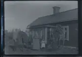 En familj med två små barn fotograferade framför sitt hus, tillsammans med sin häst. Det yngsta barnet sitter uppe på hästryggen.
