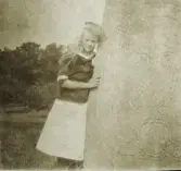 En tonårsflicka i sjömansblus lutar sig mot en runsten (?) (minnessten?).