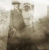 En äldre man och en ung kvinna poserar för fotografen framför ett slottsliknande hus.
Jfr Alb23-003.