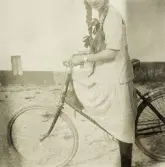 En tonårsflicka i klänning och långa flätor har stannat till på sin cykel.