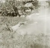 En liten flicka sitter på gräsmattan i en trädgård.