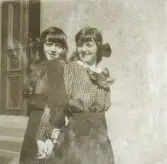 Två flickor, den ena i mörk sjömansklänning den andra i blus och kjol, poserar utanför ett bostadshus, trol. någonstans
i Växjö.