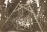 Tre unga kvinnor och en pojke i en trädgårdsgunga.
Trol. bl a t.v. Kristina Nilsson (1898-1973) och hennes bror Benno (1904-1995), Gårdsby säteri.