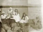 Fyra tonårsflickor i ljusa kläder har slagit sig ner på några stenar vid en sjökant (Helgasjön?).