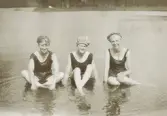 Tre glada, men blöta tonårsflickor i baddräkt och badmössa poserar för fotografen.
