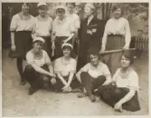 En seminarieklass med blivande lärarinnor, klädda i gymnastikdräkt (möjligen inför ett parti brännboll), har samlats för fotografen. 
Kvinnan i mörk klänning är trol. klassföreståndaren.