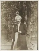 En medelålders kvinna klädd i kjol, blus och kappa. Hon håller ett par glasögon i ena handen.
Trol. seminarielärare.