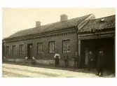 Kopparslagare Olof Olsssons verkstad vid Prästgatan 36 i Varberg. Han hade även bryggeriet Kronan. Fem män står vid byggnaden och portlidret. 1910-tal.