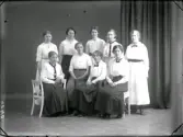 Ateljéfoto med nio unga kvinnor, möjligen en personalgrupp. De bär ljusa blusar, ett par bär slips och några fluga. Beställare: Berta Larsson.