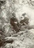 En familj har slagit sig ner på några mossbelupna stenar i en skog, trol. i närheten av Växjö.
Fr.v.: kronolänsman Albert Bergstedt, dottern Margaretha och hustrun Elisabeth, f. Eksandh.