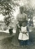 Fru Elisabeth Bergstedt med dottern Margareta i en trädgård. Till vänster syns ännu ett barn, i kolt.