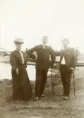 Fru Elisabeth Bergstedt, hennes make kronolänsman Albert Bergstedt och deras vän, stadsfiskal Filip Rehnström, Växjö, poserar vid en 
brygga med en ångbåt, trol. vid Evedal.