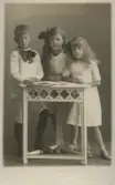 Porträtt av tre barn som står vid ett litet bord.