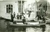 Översvämning i Bollnäs år 1916. Nygatan. Tidningar delas ut genom fönstret. Många barn hjälper till i båtarna.
