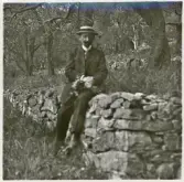 En medelålders man i kostym med stärkkrage och halmhatt sitter på en stenmur i en park. Bad Kissingen (?).
I handen har han en blombukett.
Dr. Hermann Laudien (g.m. Elsa Eksandh).