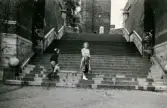 Fotografi från 1945 taget i Helsingborg, som visar Inga-Lill Börjesson som står nedanför en bred trappa. Hon har en regnkappa slängd över ena armen. 
Ovanför trapporna skymtar delar av den berömda historiska sevärdheten Kärnan.
En pojke med ljus mössa skyndar uppför trapporna. 